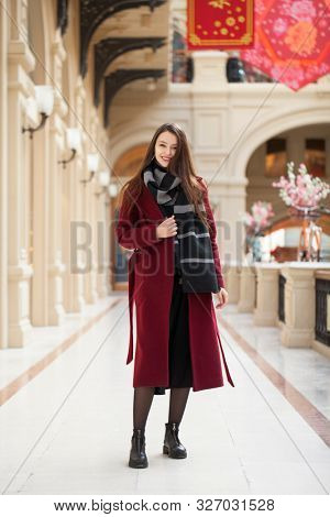 Full body portrait. Young beautiful woman in stylish in a long burgundy coat, indoor shop