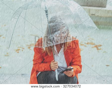 Caucasian Girl With Red Gabardine Walks Through A Park Under A Transparent Umbrella.