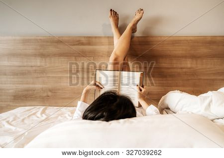 Asian Woman Lying Down, Legs Crossed, She Was Reading A Book On The Bed