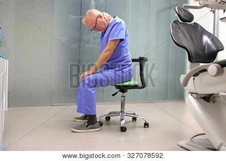 Neck pain in the dental practice.Mature dentist having short break for regeneration after long working hours in his office