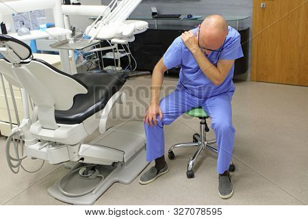 Shoulder pain in the dental practice.Mature dentist having short break for regeneration after long working hours in his office