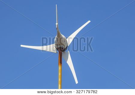 Domestic Wind Turbine Mpunted Over Metalic Pole. Blue Sky Background