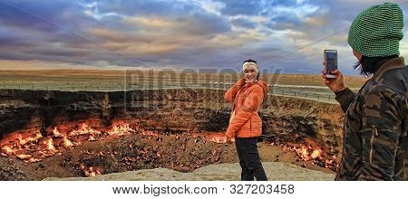 Turkmenistan, Darvaza - March 21, 2019: Girls Make A Photo On The Background Of The Burning Crater 
