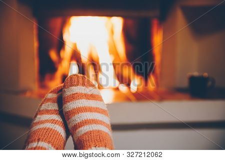 Feet In Wool Striped Socks By The Fireplace. Relaxing At Christmas Fireplace On Winter Holiday Eveni