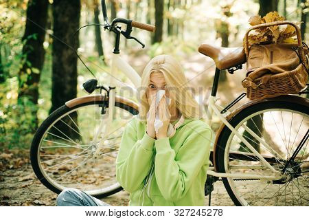Young Blonde In A Green Sweater Sitting On The Ground In The Park Blowing Her Nose On Bicycle Backgr