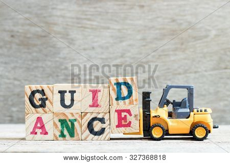 Toy Forklift Hold Letter Block D, E To Complete Word Guidance On Wood Background