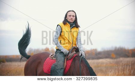 A Woman In Yellow Vest Is Sitting On A Bay Horse