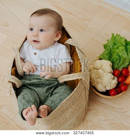 Infant Baby In A Woolven Like Bag And Bowl Of Vegetables Nearby