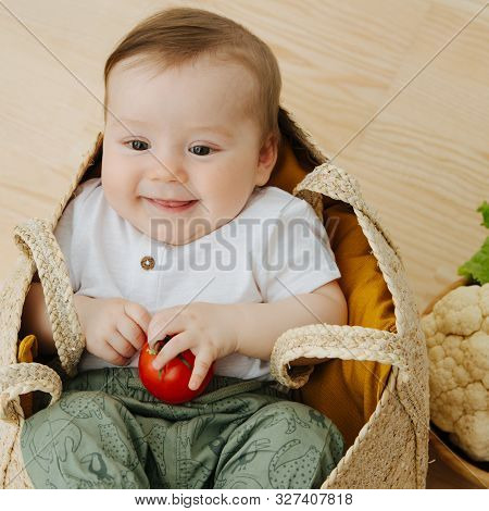 Infant Baby In A Woolven Like Bag And Bowl Of Vegetables Nearby