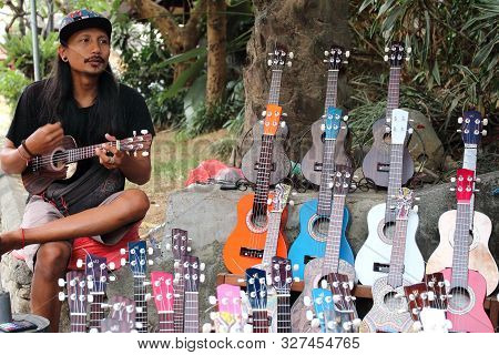 Ubud, Bali, Indonesia - August 6th Of 2019: Young Indonesian Vendor Playing The Guitar In His Souven