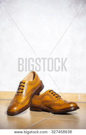 Pair Of Male Full Brogued Tan Oxford Shoes. Placed Together On Tiles Floor. Vertical Image Composiri