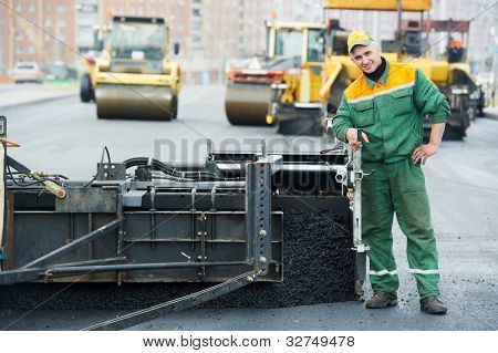 Trabajador operando la máquina pavimentadora de asfalto durante la construcción de carreteras y obras de reparación