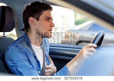 Young Brunette Man In Denim Shirt Behind Steering Wheel Of Automobile. Haggard Driver Suddenly Felt 