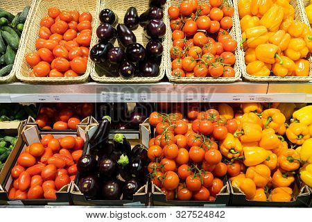 Market Counter With Wicker Baskets And Lug Boxes With Fresh Tomatoes, Squash, Orange And Yellow Pepp