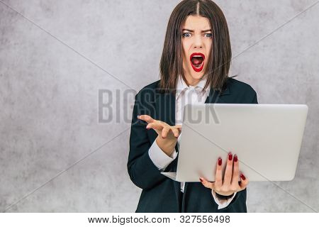 Serious Cute Businesslady Standing, Holding A Latop, Looking Angryly, Mouth Opened, Showing With Ges