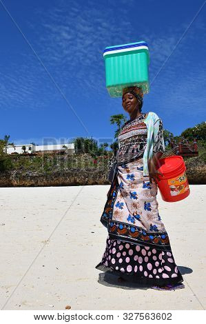 Kendwa, Zanzibar - October 3, 2019: Beautiful Local Girl In Traditional Dress Carrying A Load On Her