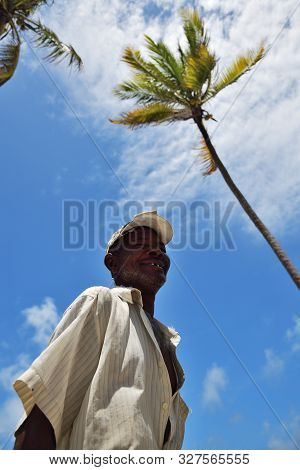 Pingwe, Zanzibar - October 6, 2019: Portrait Of The Old Local Fisherman, Blue Sky And Palms Tree On 
