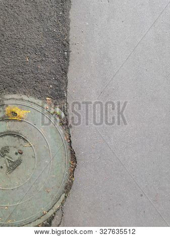 Grey Asphalt And Sunroof Background. Street Manhole In The Pavement With A Picture