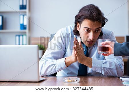 Male employee drinking alcohol and smoking cigarettes at workpla