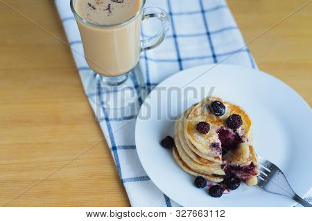 Eating Of Fritter Or Oladyi With Bramble With Fork On White Plate And Cappuccino On Table With Napki