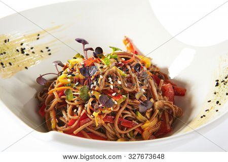 Macro shot of japanese soba, yakisoba or nagano soba with vegetables in sweet and sour sauce. Thin buckwheat noodles, pasta or tagliatelle with greens and sesame on white restaurant plate isolated