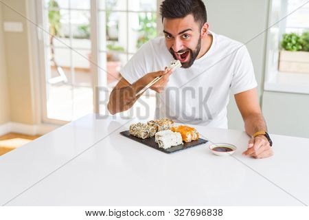 Handsome man smiling happy enjoying eating fresh colorful asian sushi using chopsticks