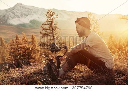 Man Sits With Electronic Gimbal And Dslr Camera Against Mountains