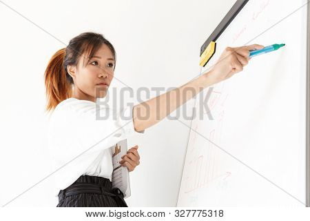 Attractive confident asian businesswoman presenting new project at the blankboard isolated over white background