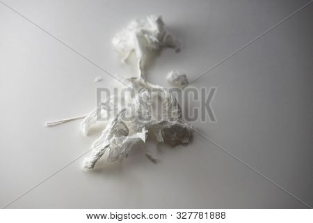 Nervous or nevously waiting. A tissue paper rolled into thin strands and ripped to bits on a white table with shadow. 