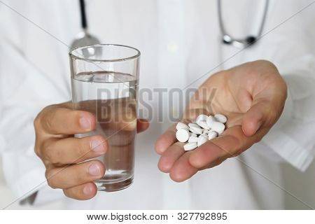 Pills And Glass Of Water In Hands Of Doctor, Physician Giving Medication In White Tablets. Concept O