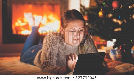 Toned Portrait Of Smiling Woman With Tablet Lying On Floor Next To Firepalce And Christmas Tree
