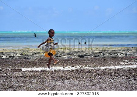 Pingwe, Zanzibar - October 6, 2019: Happy Baby Girl Dancing On Indian Ocean Coast During Low Tide. T