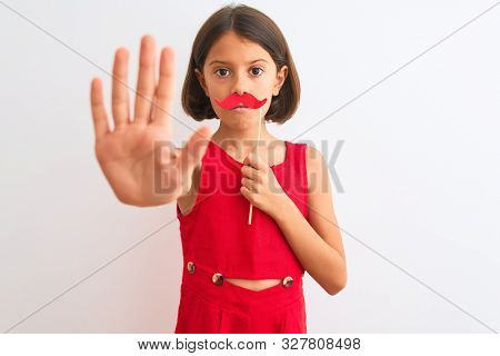 Beautiful child girl holding fanny party mustache standing over isolated white background with open hand doing stop sign with serious and confident expression, defense gesture