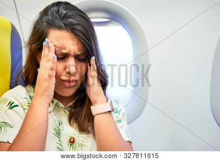 Young traveller woman sitting inside plane at the airport with sky view from the window feeling sick, headache and nauseas