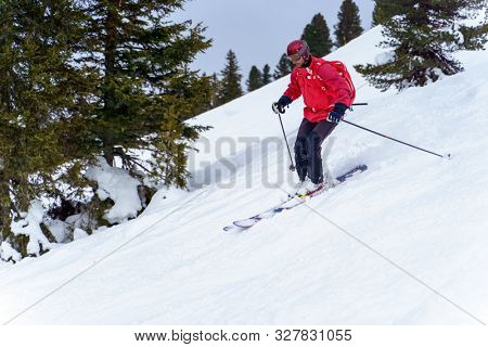 Side photo of sports man in red jacket and with backpack skiing in winter resort