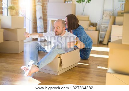 Funny and crazy couple having fun riding a cardboad box as a car, smiling happy and lauging at new home
