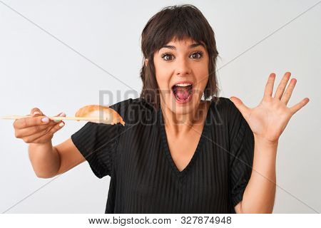 Beautiful woman eating salmon nigiri sushi using chopsticks over isolated white background very happy and excited, winner expression celebrating victory screaming with big smile and raised hands