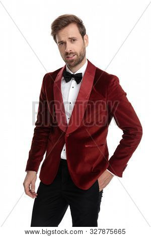 confused fashion model wearing red velvet tuxedo, holding hand in pocket, isolated on white background in studio