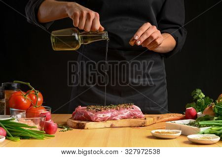 Chef Cooks Pork Steak. Pouring Oil On The Background With Vegeta