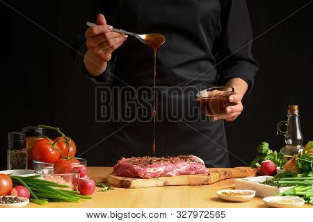 Chef Cooks Pork Steak. Pouring Sauce, Marinade On A Background W