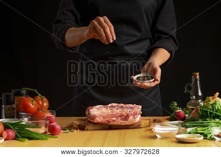 Chef Cooks Pork Ribs. Sprinkling With Pepper On A Background Wit