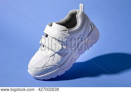 One White Childrens Sneakers With Velcro Fasteners Flying On Isolated Purple Background, Macro Sneak