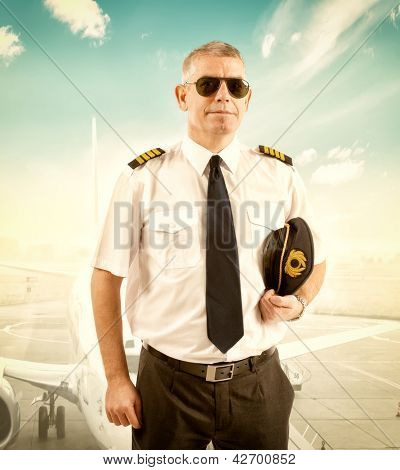 Allegro pilota indossa l'uniforme con spalline, in piedi con aereo di linea in background.