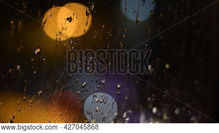 Drops Of Night Rain On Dirty Glass Window With Golden Purple Bokeh Lights Of City Traffic. Rainy Wea