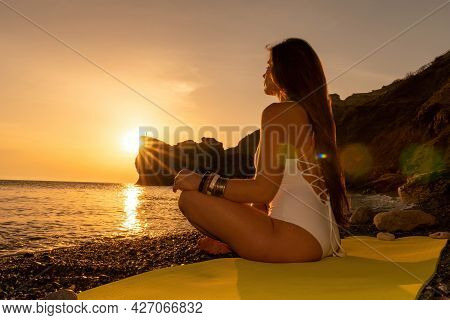 Young Woman With Long Hair In White Swimsuit And Boho Style Braclets Practicing Outdoors On Yoga Mat