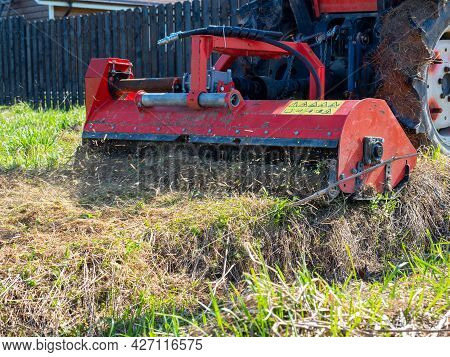 A Tractor With A Mower Attached Mulches Dry Grass Along The Fence. Land Plot Processing