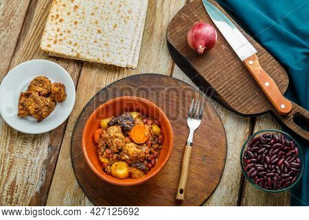 Jewish Dish Chelnt With Meat On The Table In A Plate Near Ingredients And Matzo. Horizontal Photo