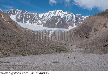 Amazing Landscape With Glacier, Mountains, Stone Valley And Hikers Walking To The Glacier Along A Mo