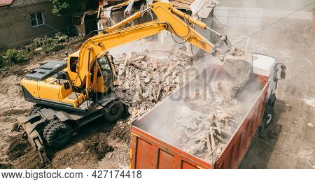 Excavator Breaks Building And Loads Construction Waste Into Truck With Its Bucket. Demolition Of Bui