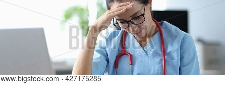 Tired Doctor Sitting At Table And Holding His Head